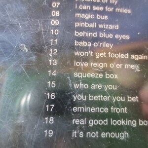 Puede incluir: Primer plano de una cinta de casete en blanco y negro con una lista de t&iacute;tulos de canciones y n&uacute;meros de pista. Los t&iacute;tulos de las canciones incluyen "I Can See For Miles", "Magic Bus", "Pinball Wizard", "Behind Blue Eyes", "Baba O'Riley", "Won't Get Fooled Again", "Love Reign O'er Me", "Squeeze Box", "Who Are You", "You Better You Bet", "Eminence Front", "Real Good Looking Boy" y "It's Not Enough".