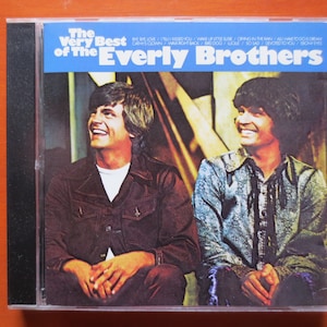 May include: A CD case with a blue background and white text that reads "The Very Best of The Everly Brothers". The image features two men, one wearing a brown jacket and the other a blue shirt, both smiling.