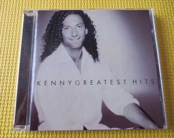 May include: A CD case featuring a black and white photograph of Kenny G on the front. The text "Kenny G Greatest Hits" is printed in white on the front of the case.