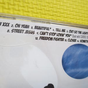 May include: A CD case with a white background and a blue sky image. The case lists the track titles for the album, including "Luv XXX", "Oh Yeah", "Beautiful", "Tell Me", "Out Go The Lights", "Street Jesus", "Can't Stop Lovin' You", "Freedom Fighter", "Closer", and "Something".