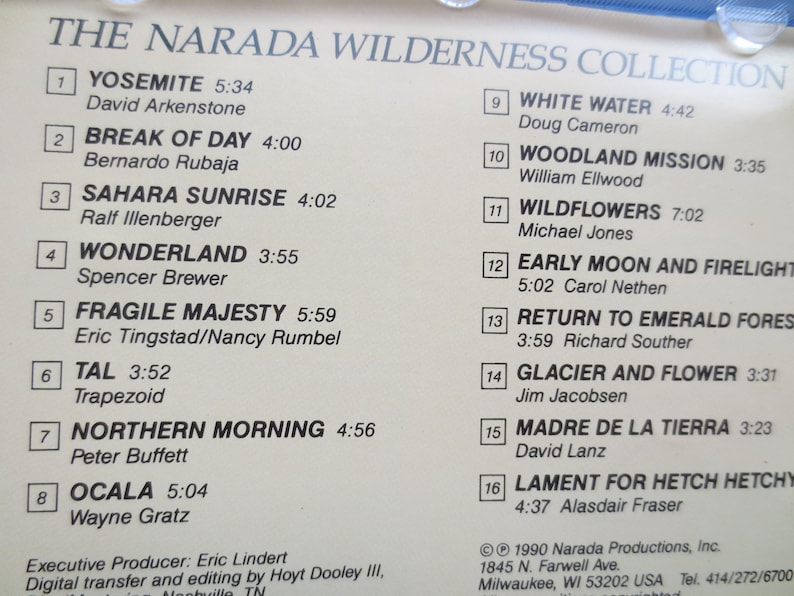 May include: A white and black album cover with the title "The Narada Wilderness Collection". The cover lists 16 songs with titles and artists, including "Yosemite" by David Arkenstone, "Break of Day" by Bernardo Rubaja, and "White Water" by Doug Cameron. The album cover also includes the copyright information for Narada Productions, Inc.