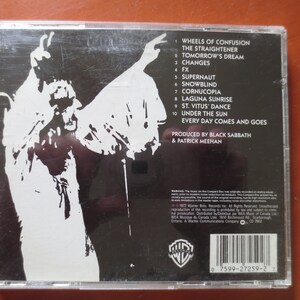 May include: Black and white CD case back with a silhouette of a person with their arms raised. The text on the back lists the songs on the album "Wheels of Confusion" by Black Sabbath. The album was produced by Black Sabbath and Patrick Meehan.