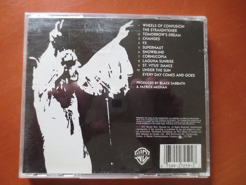 May include: Black and white CD case back with a silhouette of a person with their arms raised. The text on the back lists the songs on the album "Wheels of Confusion" by Black Sabbath. The album was produced by Black Sabbath and Patrick Meehan.