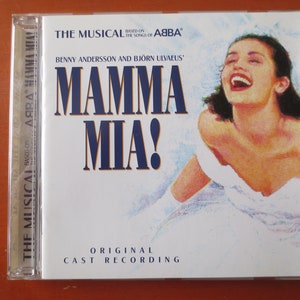 May include: A white CD case with a blue and yellow title, "MAMMA MIA!" The musical is based on the songs of ABBA by Benny Andersson and Bjorn Ulvaeus. The case features a woman with dark hair smiling and wearing a white dress.