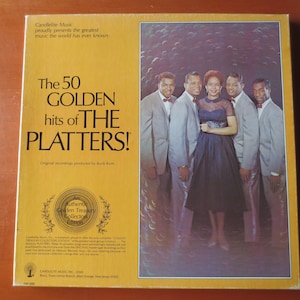 Könnte beinhalten: Ein gelbes und oranges Schallplattenalbumcover mit einer Gruppe von fünf Sängern, darunter eine Frau in einem schwarzen Kleid. Der Albumtitel lautet "The 50 Golden Hits of The Platters!" mit dem Text "Original recordings produced by Buck Ram".
