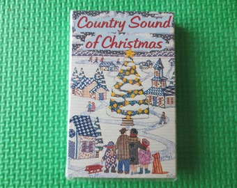 May include: A cassette tape with a colorful illustration of a snowy winter scene with a family standing in front of a large Christmas tree. The text on the cassette tape reads "Country Sound of Christmas".