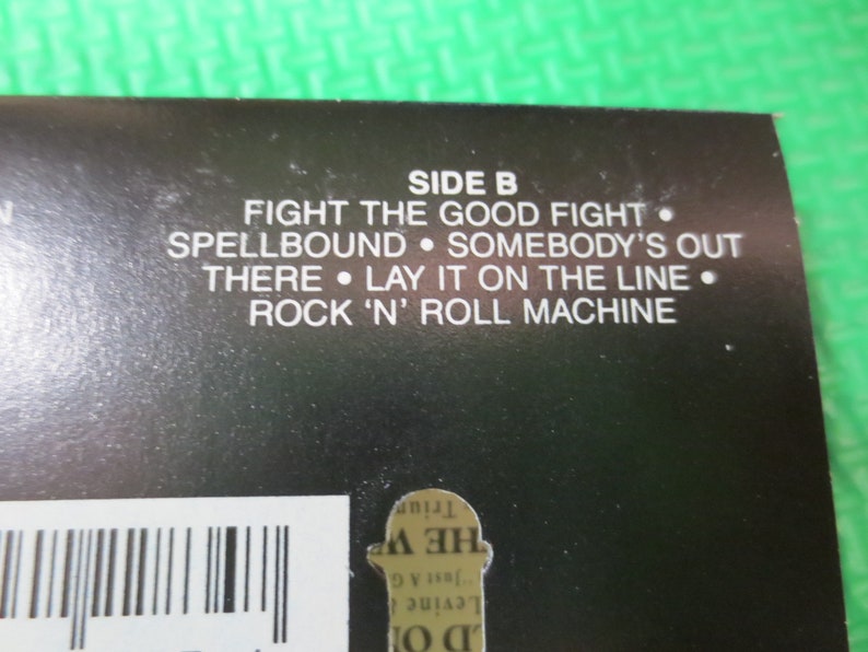 Puede incluir: Portada de &aacute;lbum en blanco y negro con el texto "SIDE B" y una lista de t&iacute;tulos de canciones: "Fight the Good Fight", "Spellbound", "Somebody's Out", "There", "Lay It on the Line" y "Rock 'n' Roll Machine".