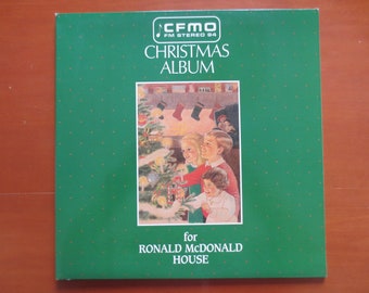 May include: A green record album cover with the text "CFMO FM Stereo 84 Christmas Album for Ronald McDonald House". The cover features a Christmas scene with a decorated tree, children, and stockings.