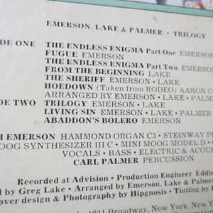 May include: Black and white record album cover for Emerson, Lake & Palmer's "Trilogy" album. The album cover features the band's name and the album title in white text on a black background. The track listing for each side of the album is also included. The album was recorded at Advision and produced by Emerson, Lake & Palmer. The album was arranged by Hipgnosis and the cover design and photography were done by Hipgnosis.