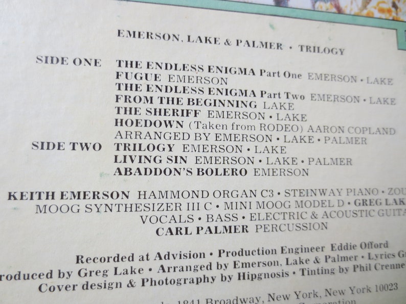 May include: Black and white record album cover for Emerson, Lake & Palmer's "Trilogy" album. The album cover features the band's name and the album title in white text on a black background. The track listing for each side of the album is also included. The album was recorded at Advision and produced by Emerson, Lake & Palmer. The album was arranged by Hipgnosis and the cover design and photography were done by Hipgnosis.