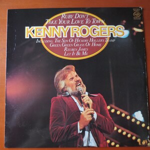 Peut inclure: Une pochette d'album vinyle de Kenny Rogers, un chanteur de musique country. La pochette de l'album est noire avec un cercle doré au centre. Le cercle contient le titre de l'album "Ruby Don't Take Your Love To Town" et la liste des pistes de l'album. La pochette de l'album présente une photo de Kenny Rogers chantant dans un microphone.