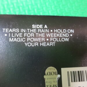 Puede incluir: Caja de cassette negra con texto blanco que enumera las canciones del lado A: "Tears in the Rain", "Hold On", "I Live for the Weekend", "Magic Power" y "Follow Your Heart".