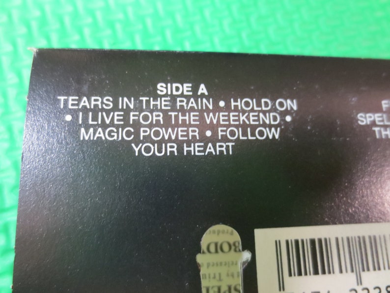 Puede incluir: Caja de cassette negra con texto blanco que enumera las canciones del lado A: "Tears in the Rain", "Hold On", "I Live for the Weekend", "Magic Power" y "Follow Your Heart".