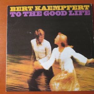 Può includere: Una copertina di un album in vinile vintage con una coppia che balla in un'acqua bassa. La copertina dell'album è intitolata "BERT KAEMPTFERT TO THE GOOD LIFE".