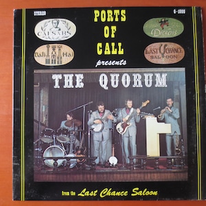 May include: A vintage vinyl record album cover featuring a band called "The Quorum" performing live at the "Last Chance Saloon". The album is titled "Ports of Call presents The Quorum".