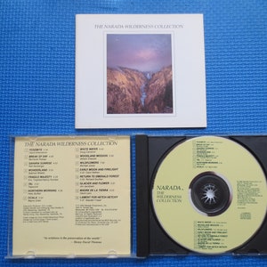 May include: A CD case with a yellow CD inside. The CD case has a white background with black text that reads "The Narada Wilderness Collection". The CD has a yellow background with black text that reads "Narada. The Wilderness Collection".