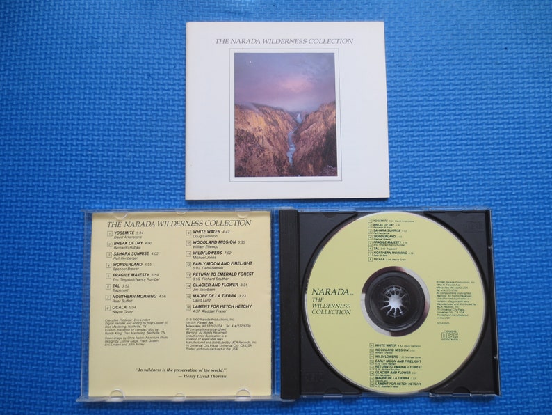 May include: A CD case with a yellow CD inside. The CD case has a white background with black text that reads "The Narada Wilderness Collection". The CD has a yellow background with black text that reads "Narada. The Wilderness Collection".