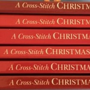 May include: A stack of six red books titled A Cross-Stitch Christmas by Craftways. The spines feature individual titles: A Season to Remember, Handmade Memories, A Heartwarming Holiday, Seasonal Sensations, Holiday Celebrations, and Treasured Memories.