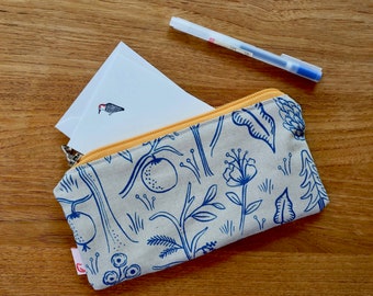May include: A gray and white zippered pouch with a blue floral pattern. The pouch is open and a white card with a small bird illustration is inside. A clear pen is lying on a wooden surface.