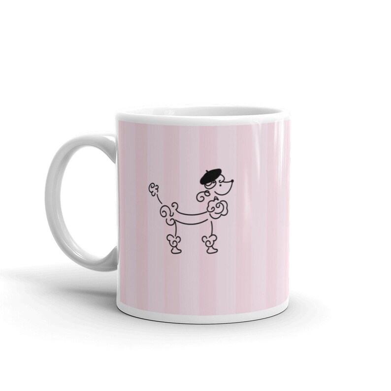 May include: White ceramic mug with a pink and white striped design. A black and white illustration of a poodle wearing a beret is centered on the mug.