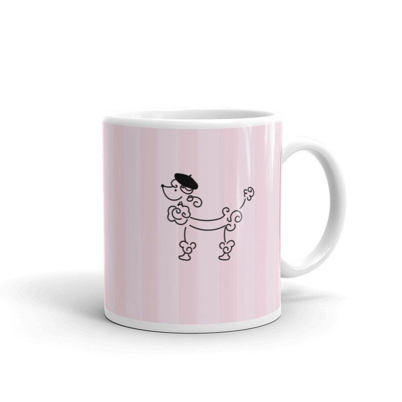 May include: White ceramic mug with a pink and white striped background. A black line drawing of a poodle wearing a beret is centered on the mug.