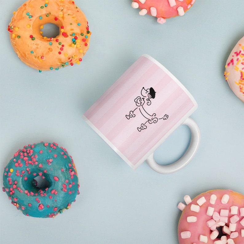 May include: White ceramic mug with a pink and white striped design. A black line drawing of a poodle wearing a beret is on the mug.
