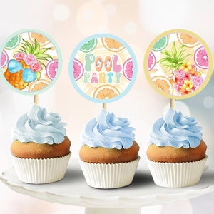 Może przedstawiać: Trzy niebieskie, lukrowane babeczki z białymi papierowymi foremkami. Każda babeczka ma okrągły, kolorowy papierowy topper z tropikalnym wzorem owoców i ananasa. Toppery mówią "Pool Party".