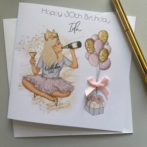 May include: A birthday card with a pink and gold illustration of a woman wearing a crown and a "Birthday Girl" shirt. The card says "Happy 30th Birthday Ida".