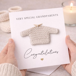 May include: A white greeting card featuring the text VERY SPECIAL GRANDPARENTS at the top and Congratulations in script below. A small, cream-coloured crocheted jumper with two wooden knitting needles is attached to the centre of the card.