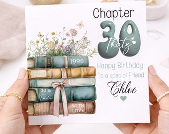Puede incluir: Tarjeta de cumpleaños con una pila de libros y detalles florales. La tarjeta dice "Capítulo 30" y "Feliz cumpleaños a un amigo especial Chloe". Los libros son de color verde azulado y marrón con una cinta rosa.