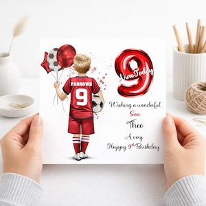 May include: A birthday card with a cartoon illustration of a boy in a red football kit, holding balloons and a football. The card reads "Nine Today" and "Happy 9th Birthday". The card is held by two hands.