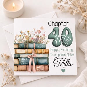 Può includere: Un biglietto di compleanno con il testo "Capitolo 40" e "Buon compleanno a una sorella speciale Millie". La carta presenta una pila di libri con accenti floreali e farfalle. La carta ha un nastro rosa e il testo "40 & Fabulous" e "With Love".