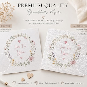 May include: Two square white greeting cards featuring a floral wreath illustration with pink hearts and the text Just For You. One card displays a linen finish with a subtle woven texture, while the other shows a hammered finish with a textured surface.