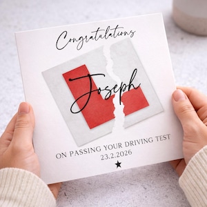 Peut inclure: Une carte de vœux carrée blanche avec le texte Congratulations en écriture noire en haut. Au centre, un L rouge sur un fond carré blanc déchiré avec le nom Joseph en écriture noire. En dessous, ON PASSING YOUR DRIVING TEST 23.2.2026 et une étoile.