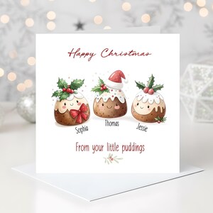 Pode incluir: Cartão de Natal branco com o texto "Happy Christmas" e "From your little puddings". O cartão apresenta três pudins de Natal de desenho animado, cada um com um design e um nome únicos: Sophia, Thomas e Jessie.
