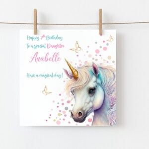 May include: A white unicorn with a gold horn and a rainbow mane and tail. The unicorn is surrounded by pink, gold, and gray confetti. The text "Happy 7th Birthday To a special Daughter Anabelle Have a magical day!" is written on the card.