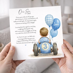 Puede incluir: Tarjeta de felicitación con una ilustración en acuarela de un niño en un coche de carreras azul, sosteniendo globos azules. La tarjeta tiene un poema sobre el tercer cumpleaños de un niño, con el texto "Our Son" en la parte superior.