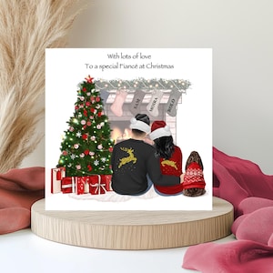 Op de afbeelding: Een kerstkaart met een feestelijke scène. Het toont een versierde kerstboom, een open haard met kousen en een stel met kerstmutsen. De tekst op de kaart luidt "With lots of love To a special Fiancé at Christmas."