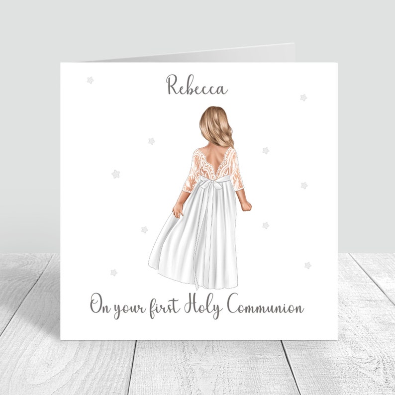 May include: A white greeting card with an illustration of a girl in a white dress with lace sleeves and back. The card has the name "Rebecca" at the top and the text "On your first Holy Communion" at the bottom. Small star shapes are scattered around the illustration.