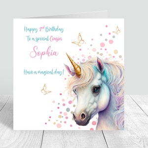 May include: A white unicorn with a gold horn and a blue and pink mane. The unicorn is surrounded by pink, gold, and gray confetti and butterflies. The text "Happy 2nd Birthday To a special Cousin Sophia Have a magical day!" is written on the card.