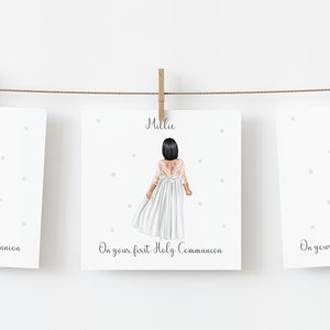 May include: Three framed illustrations of girls in white dresses, hanging from a string with wooden clips. Each illustration features a girl with a different hair color and the text "On your first Holy Communion". The names Lily, Millie, and Rebecca are above each illustration.