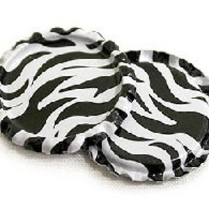 May include: Two bottle caps with a black and white zebra stripe pattern. The caps are round with a crimped edge, and the zebra stripes are irregular and bold. The caps are on a white background.