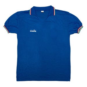 May include: A royal blue polo shirt with a V-neck collar. The collar and sleeve cuffs have red, white, and green stripes. A small white logo is on the chest. The shirt is likely made of a breathable fabric.