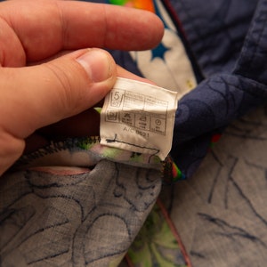 May include: Close-up of a section of patterned fabric, featuring a tag with care instructions. The fabric has a dark blue background with a floral and star design, and a colorful border.