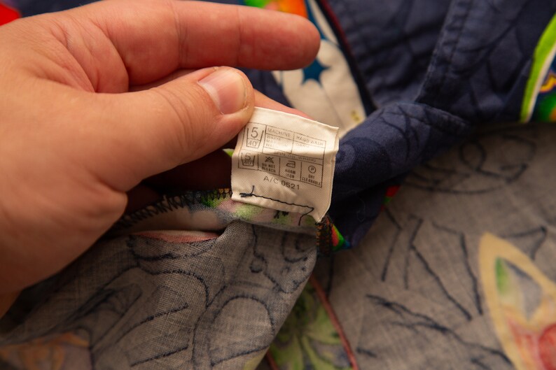 May include: Close-up of a section of patterned fabric, featuring a tag with care instructions. The fabric has a dark blue background with a floral and star design, and a colorful border.