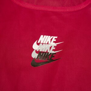May include: A close-up of a red athletic top featuring the Nike logo. The logo is stacked three times, with the top logo in white, the middle in grey, and the bottom in black.