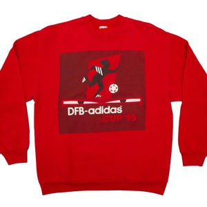Op de afbeelding: Rood sweatshirt met lange mouwen met een zwart-witte afbeelding van een voetballer en de tekst "DFB-adidas Cup '95".