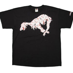 Könnte beinhalten: Schwarzes T-Shirt mit einer weißen und roten Grafik eines springenden Tieres. Das Shirt hat einen Rundhalsausschnitt und kurze Ärmel. Das Wort "CONVERSE" ist in Weiß auf dem rechten Ärmel aufgedruckt.