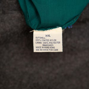 May include: A close-up of a tag with the text "XXL" and details about the garment's materials: 100% coated nylon outshell and 100% polyester lining. The tag also includes the RN number and the text "MADE IN HONG KONG".