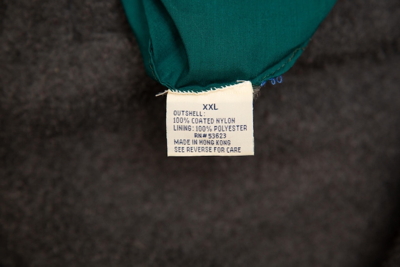 May include: A close-up of a tag with the text "XXL" and details about the garment's materials: 100% coated nylon outshell and 100% polyester lining. The tag also includes the RN number and the text "MADE IN HONG KONG".